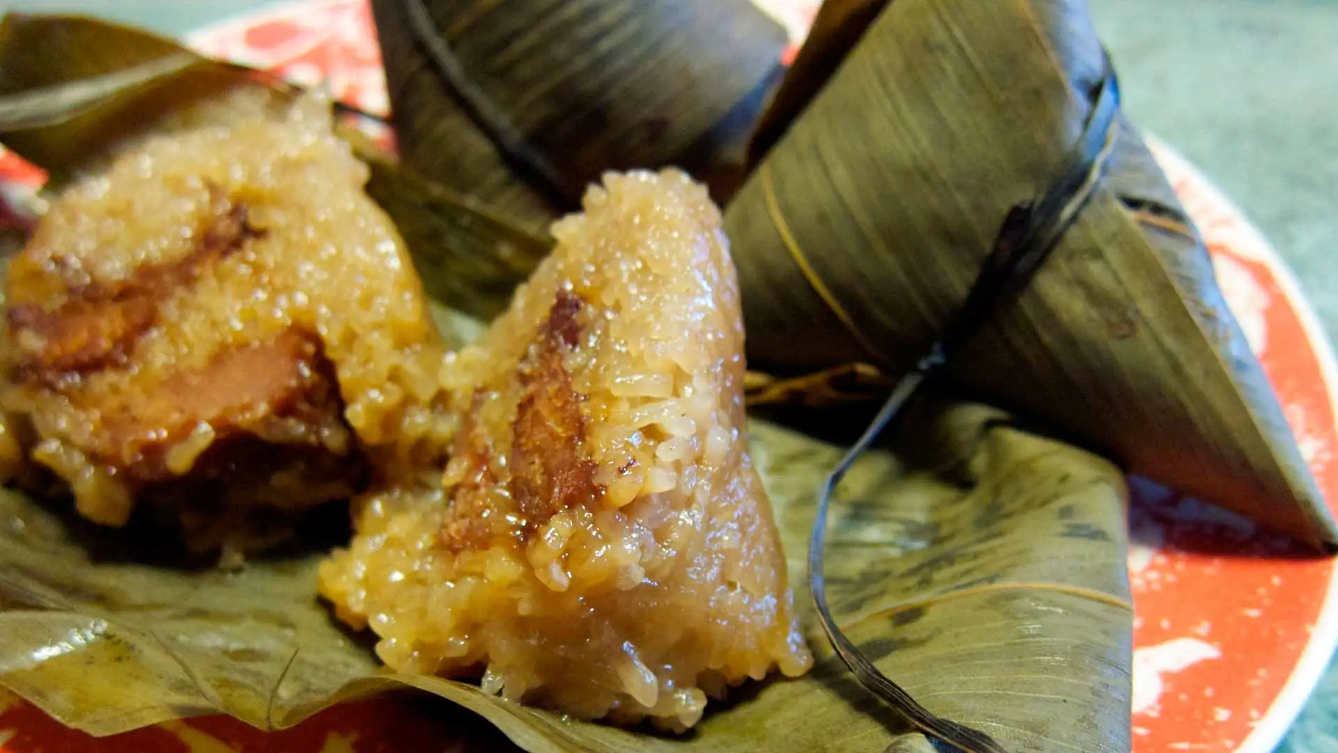zongzi es un popular triángulo de arroz glutinoso relleno de carne o judías dulces y enrollado con hojas de bambú